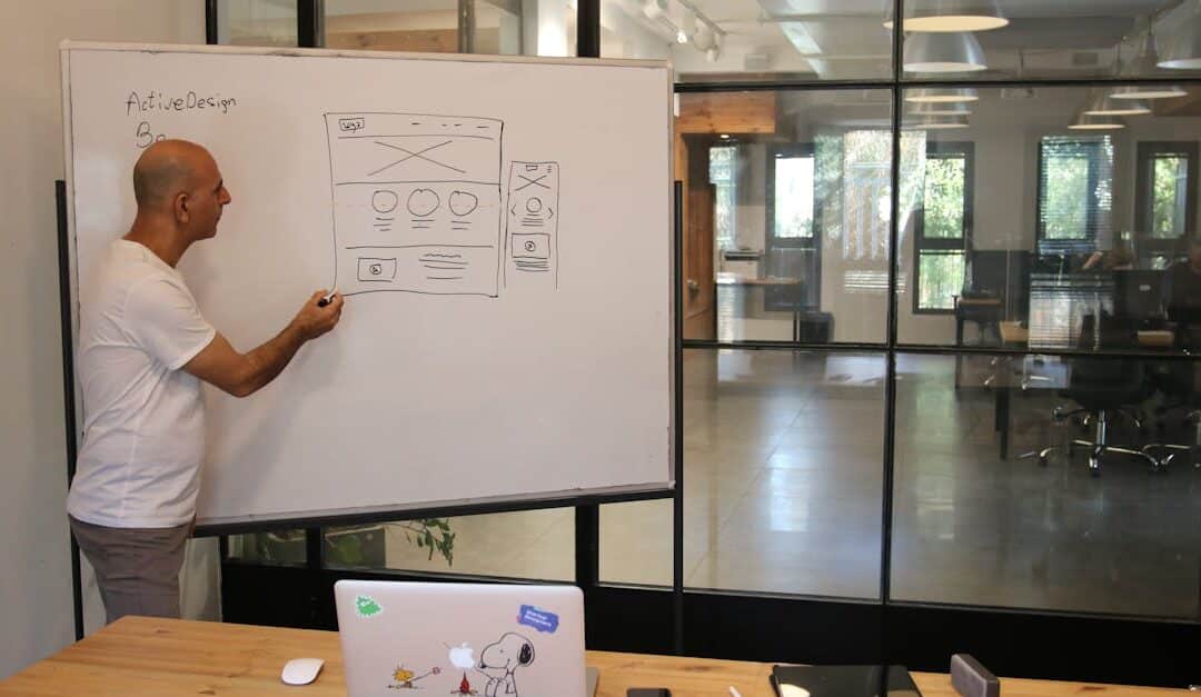 Side view of adult male manager in white t shirt standing near whiteboard and explaining business strategy during work in modern office