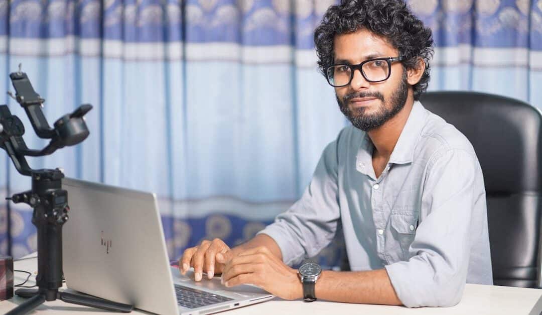 Portrait of a web developer with a laptop and camera, working at his office desk in a modern setup.