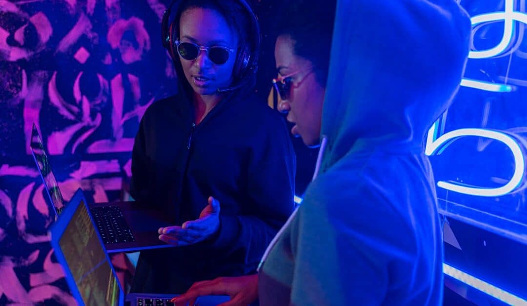 Two people using laptops in a neon-lit room, discussing technology concepts.