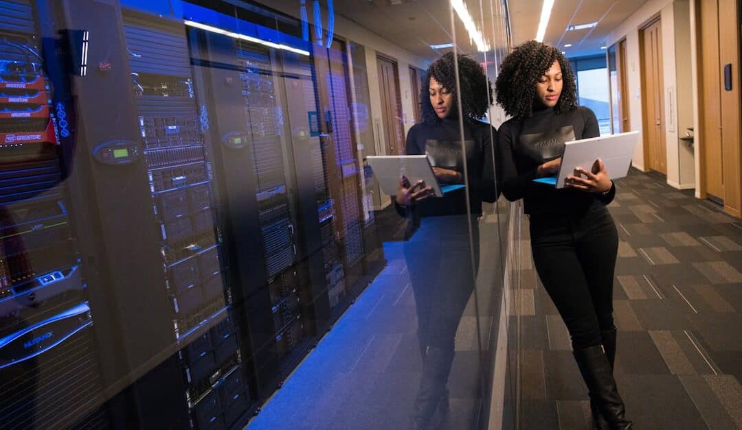 A woman using a laptop navigating a contemporary data center with mirrored servers.
