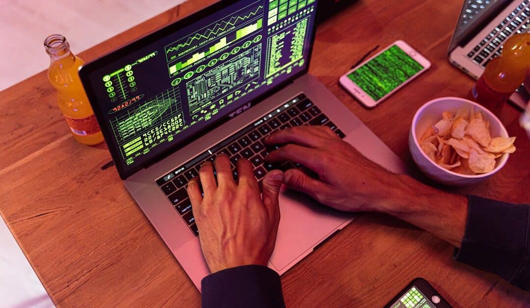 Hands typing on a laptop with coding, phone on desk, symbolizing cybersecurity.