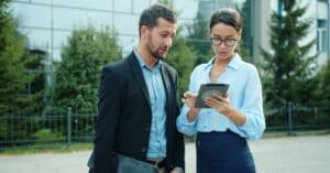 Professional colleagues discussing work on a tablet outdoors in an urban setting.